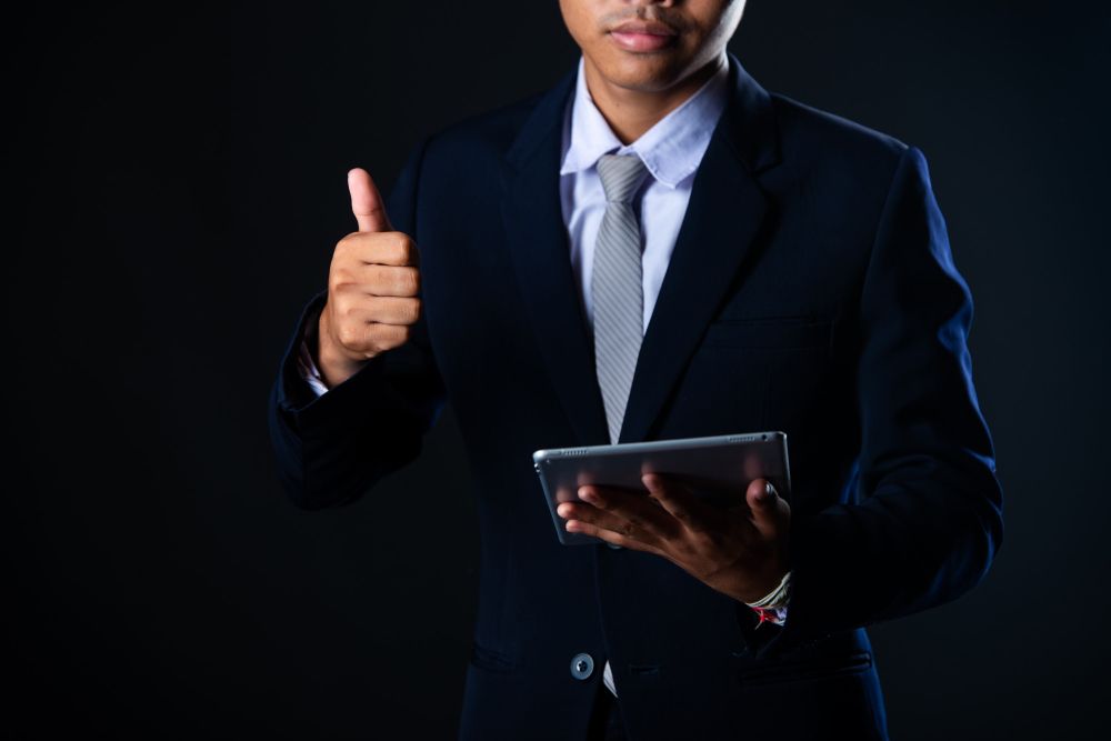 Businessperson holding a tablet and giving a thumbs-up against a dark background