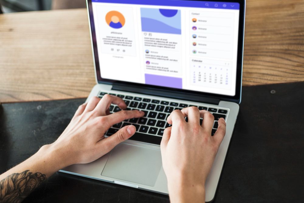 Hands typing on a laptop showing a dashboard dashboard with charts and a sidebar on a wooden desk