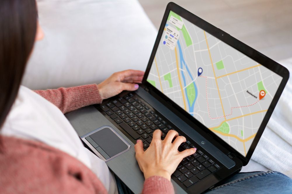 Person using a laptop with a map open, planning a route on a couch.