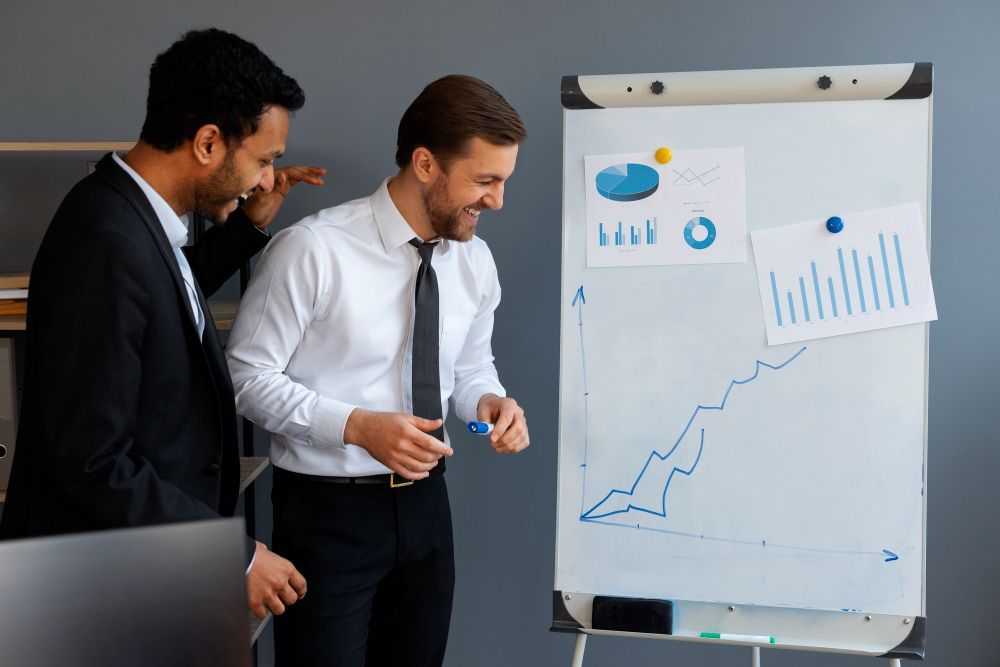 Two professionals reviewing a rising sales chart on a flip chart in an office meeting