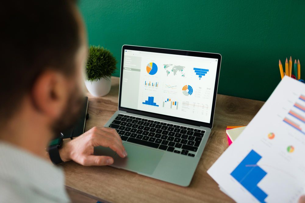 Person viewing analytics dashboard on laptop at a desk with papers and pencils
