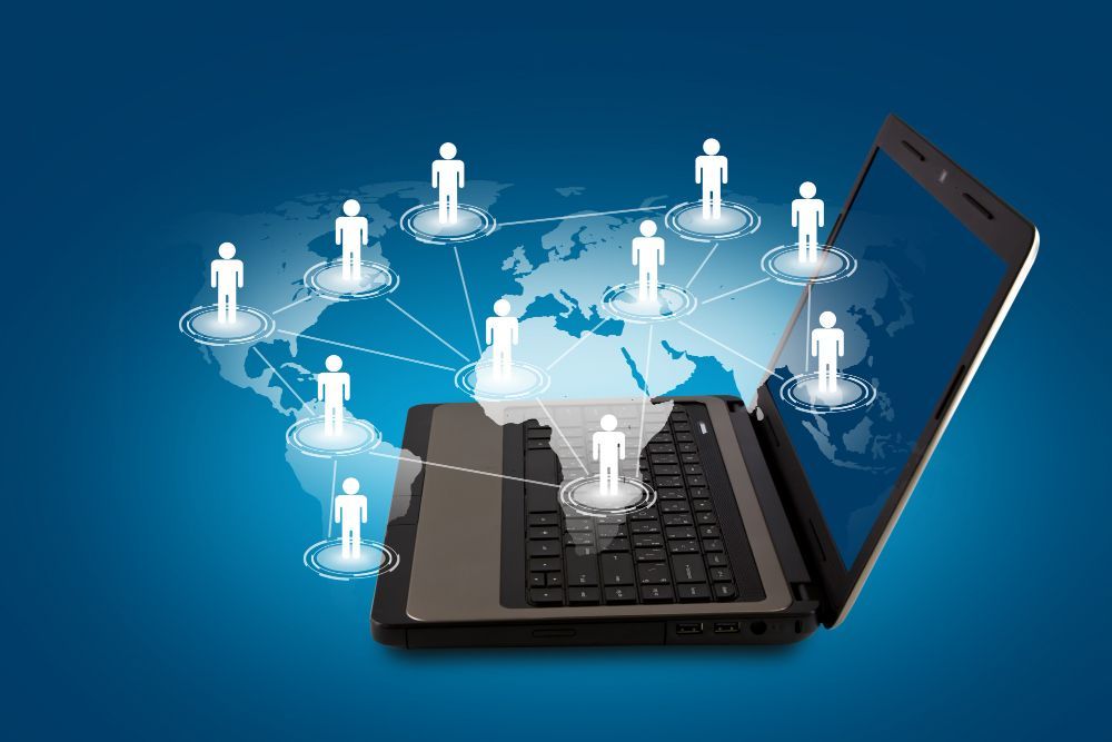 Laptop with glowing network icons connecting to people silhouettes on a blue digital background