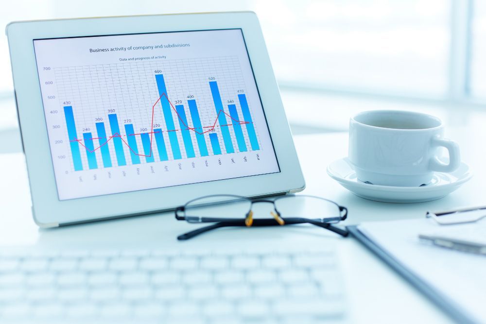 Laptop displaying a blue bar chart beside glasses and a coffee cup on a bright desk