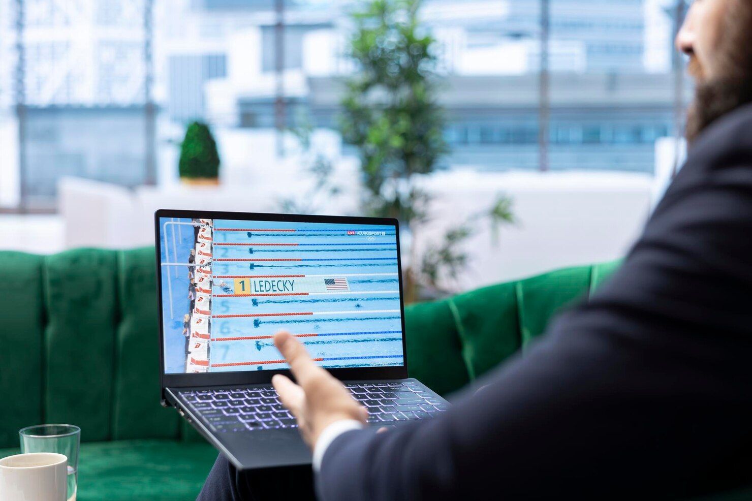 Person using a laptop on a green couch in a bright office, with a video call or chat open on screen