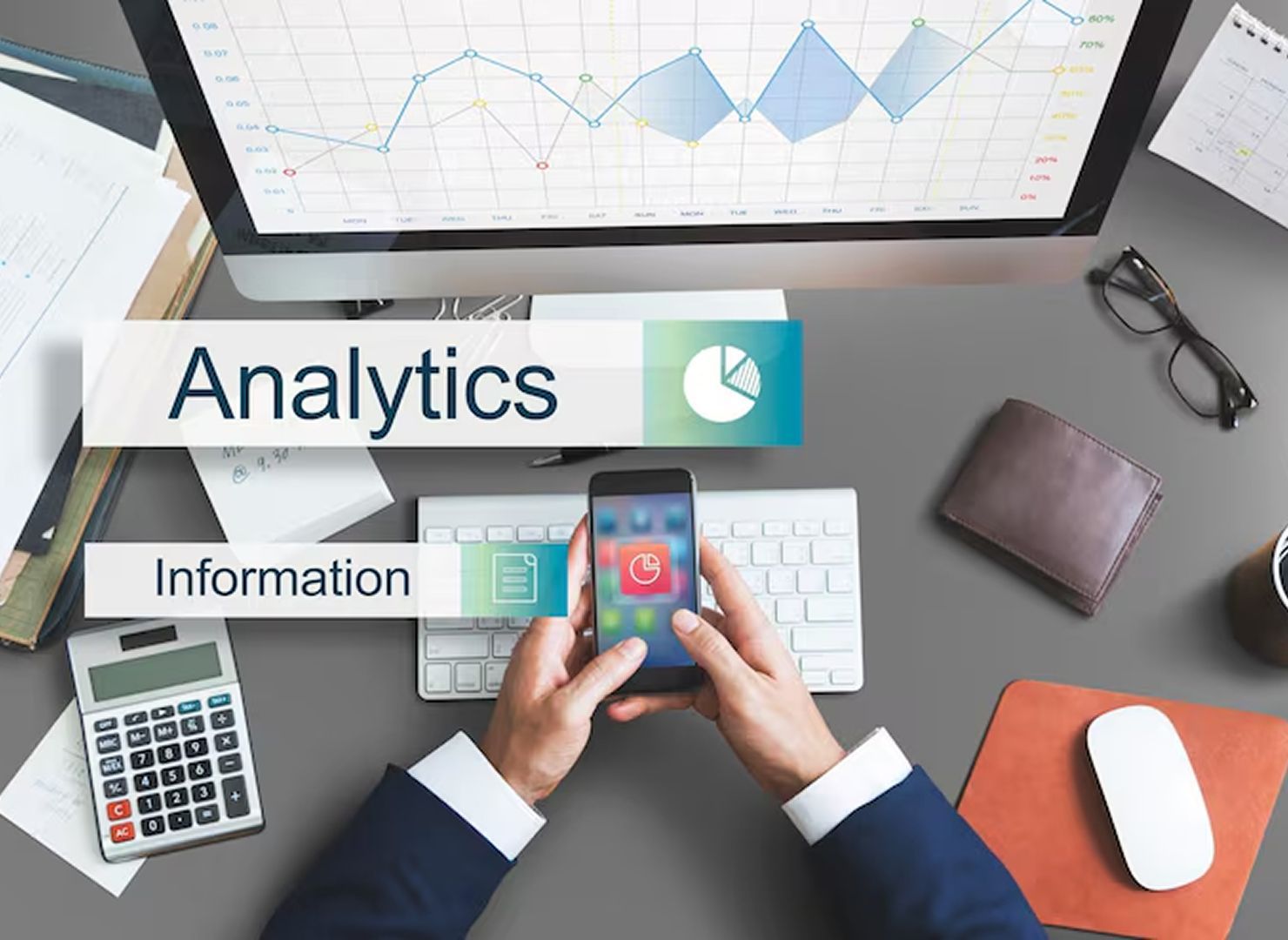 Desk with analytics charts, calculator, keyboard, and hands holding a smartphone under