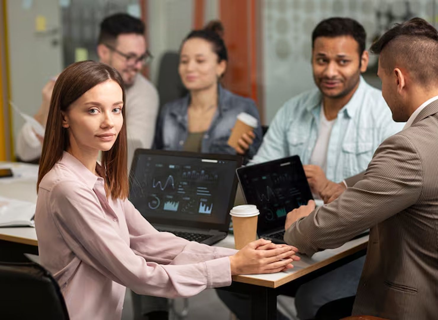 Team meeting around a laptop in a conference room, with charts on the screen and coffee cups on the table.