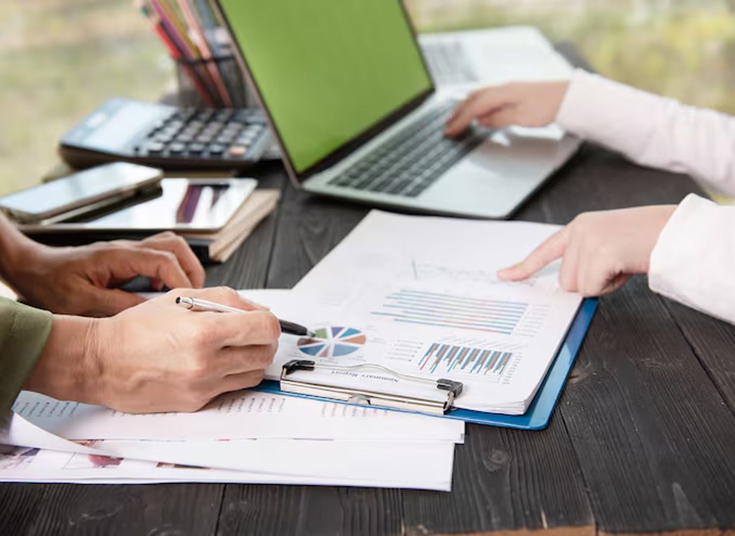 People reviewing documents at a desk with a laptop and clipboard