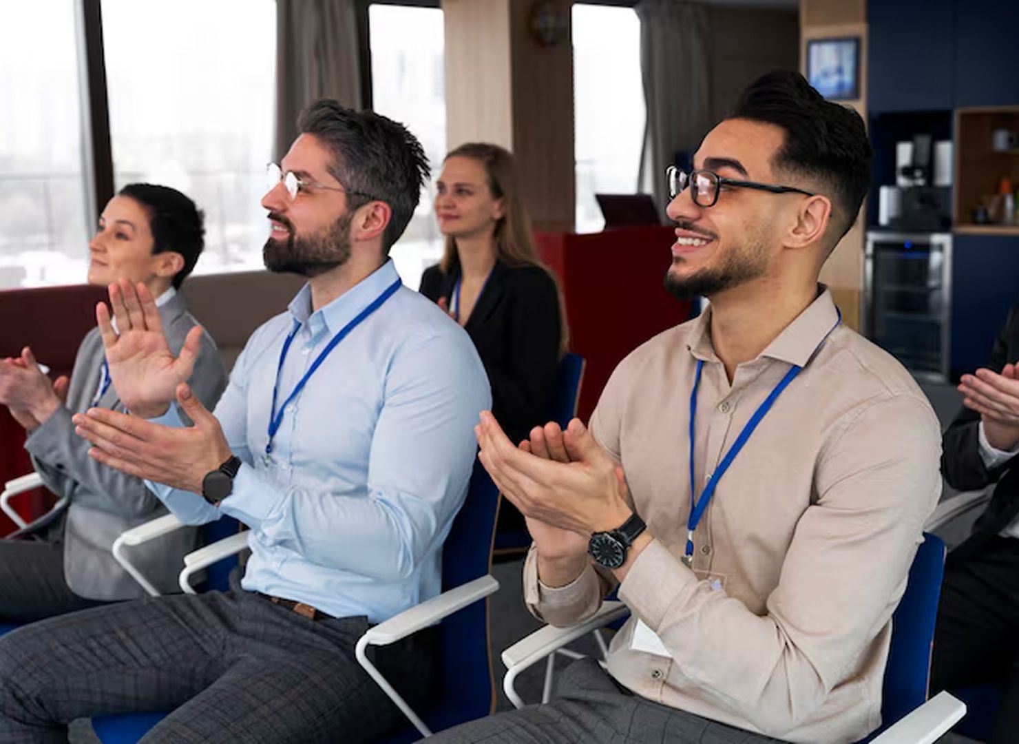 Audience members applauding at a conference, seated in a meeting room with lanyards on