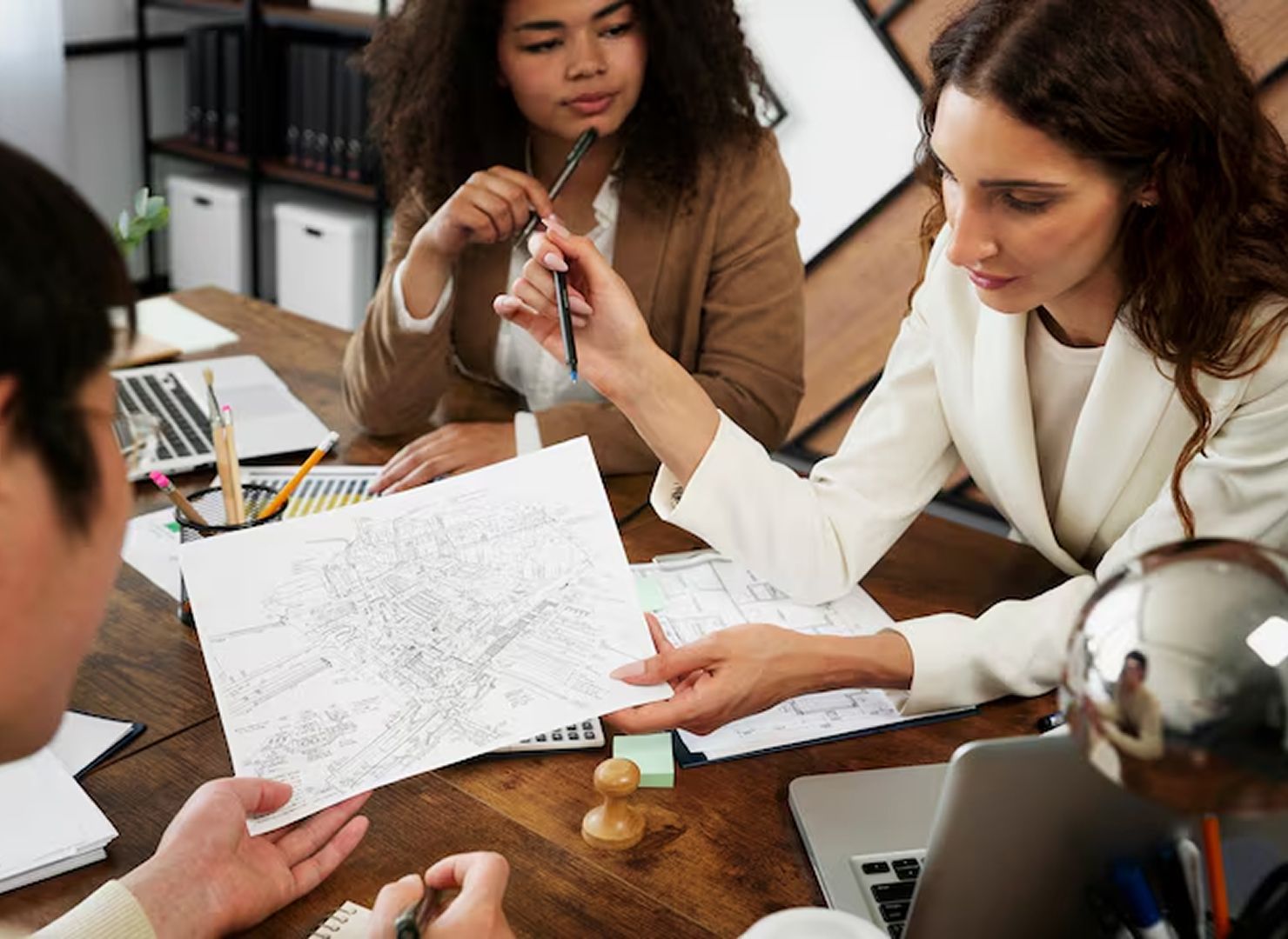 People collaborating around a table, reviewing documents and pointing at a chart in an office meeting.