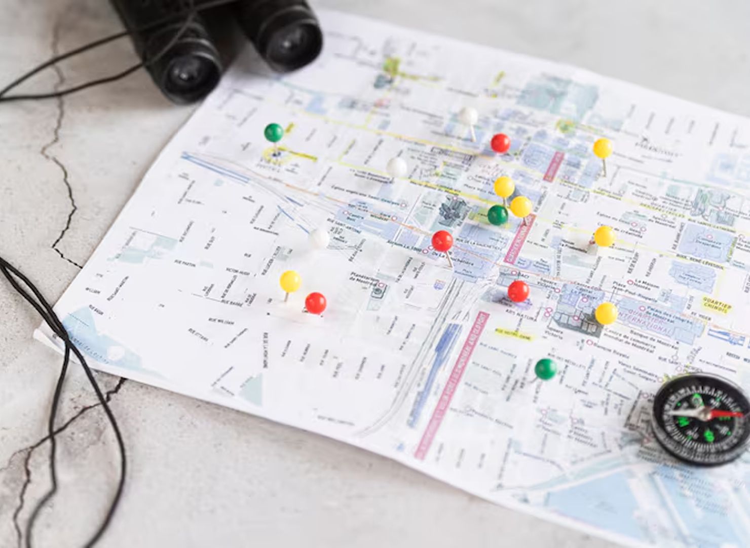 Map with colorful pins, binoculars, and a compass on a table