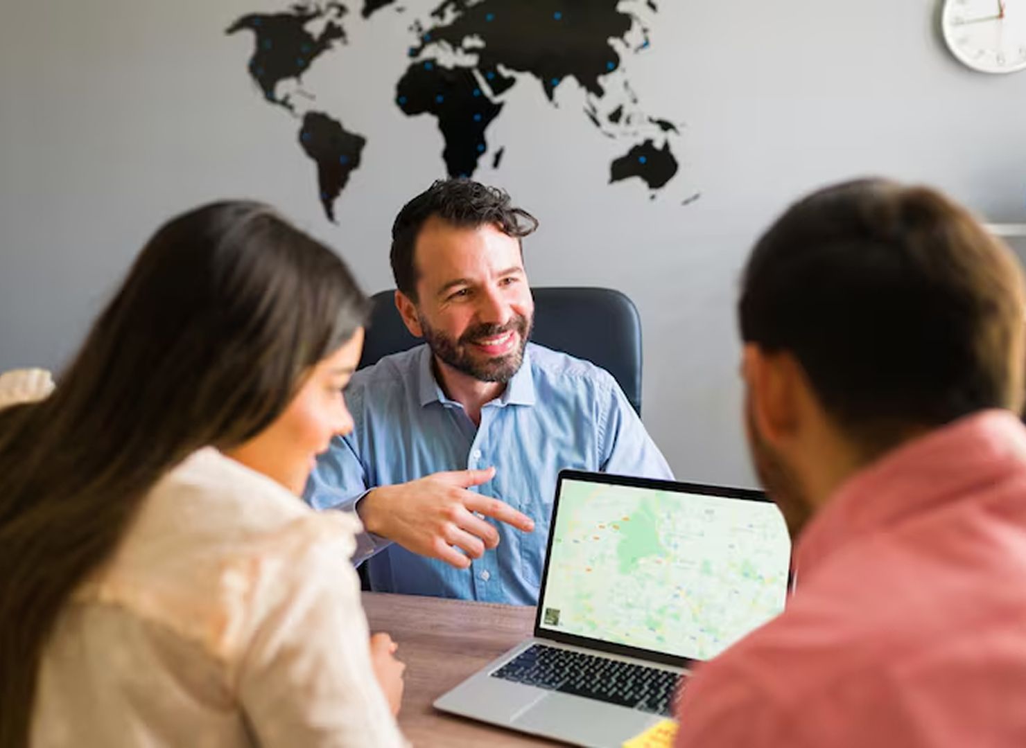 Business meeting with three people around a laptop, discussing a map on the screen.