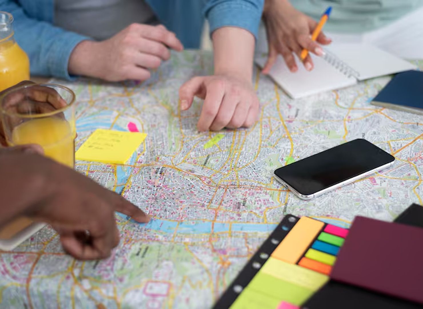 Hands pointing at a colorful map with sticky notes, a smartphone, and markers on a table