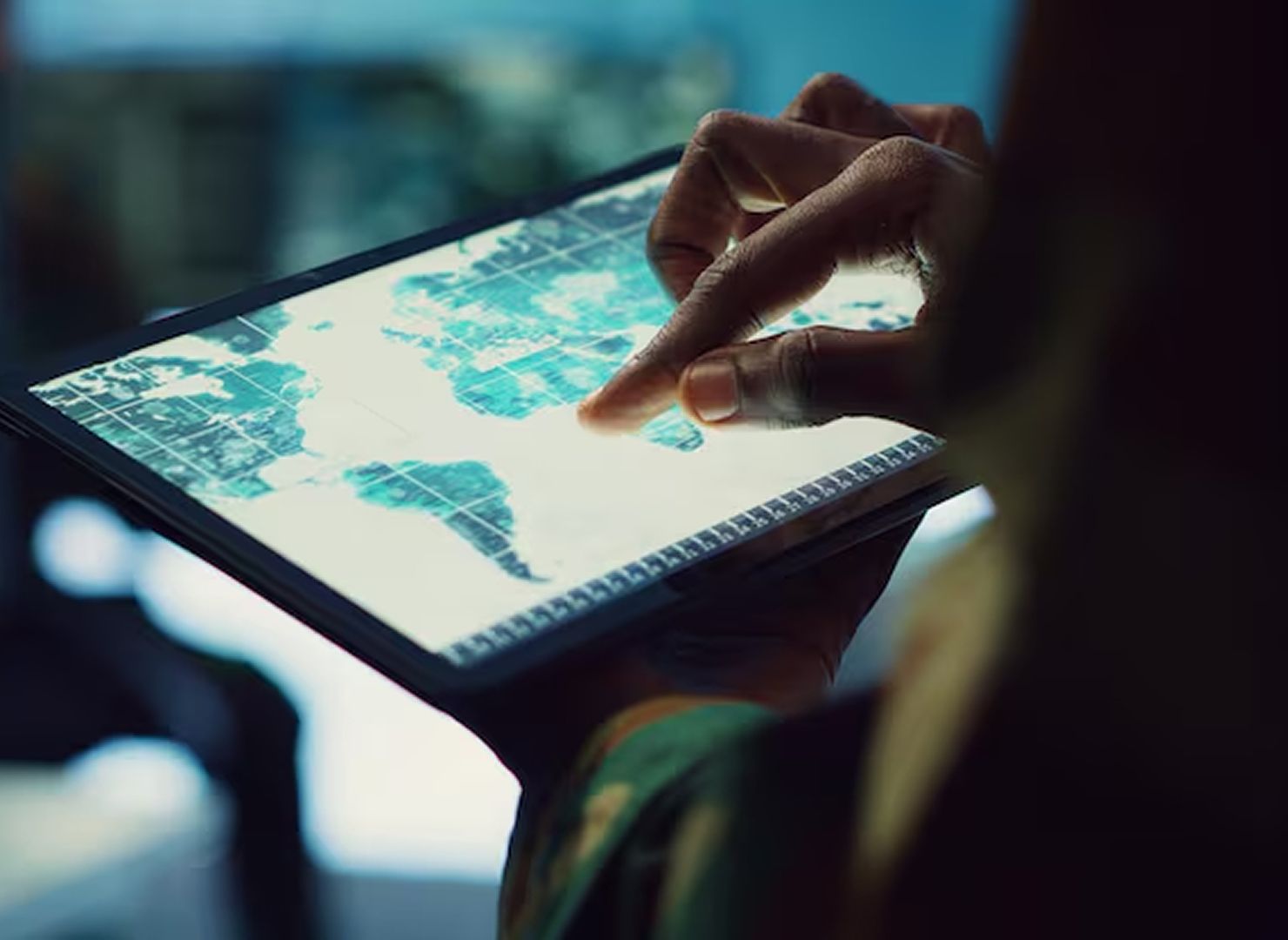 Hand touching a tablet displaying a world map on a dark desk