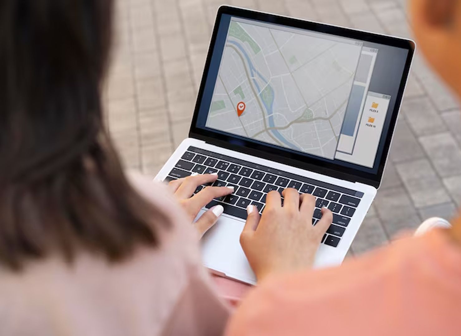 Person using a laptop with a map app on the screen, typing on a bench outdoors