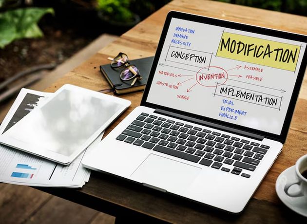 Laptop showing a handwritten planning board with notes, next to a tablet and coffee on a wooden table