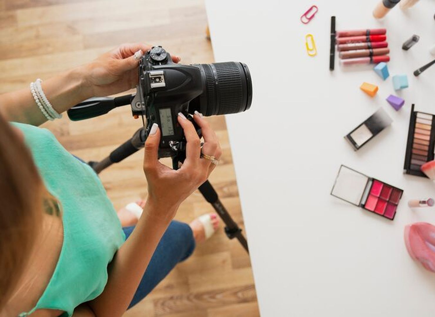 Person holding a DSLR camera over a desk with colorful makeup products arranged on the right