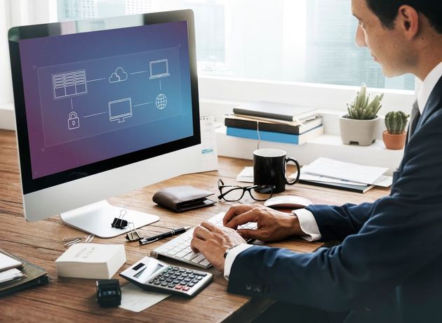 Man working at desk with laptop, papers, calculator, and coffee mug in a bright office.