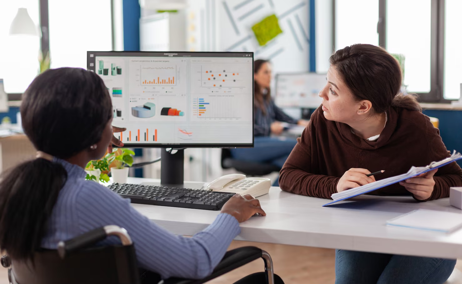 Two people discussing charts on a desktop monitor in an office setting