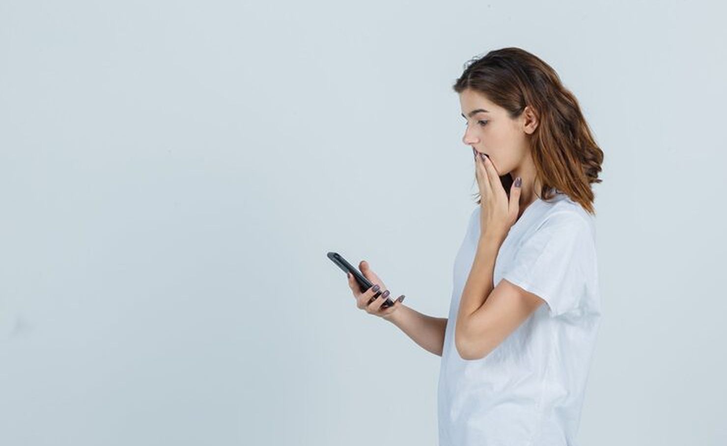 Woman in a white shirt looking at her phone with a thoughtful expression against a plain background
