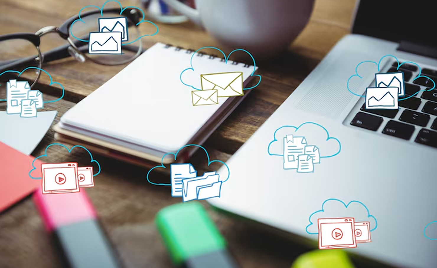 Laptop, notebook, and coffee on a desk with floating email and cloud icons, suggesting online communication.