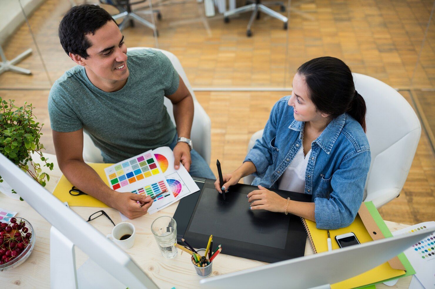 Two coworkers reviewing a color chart at a desk, smiling in a bright office