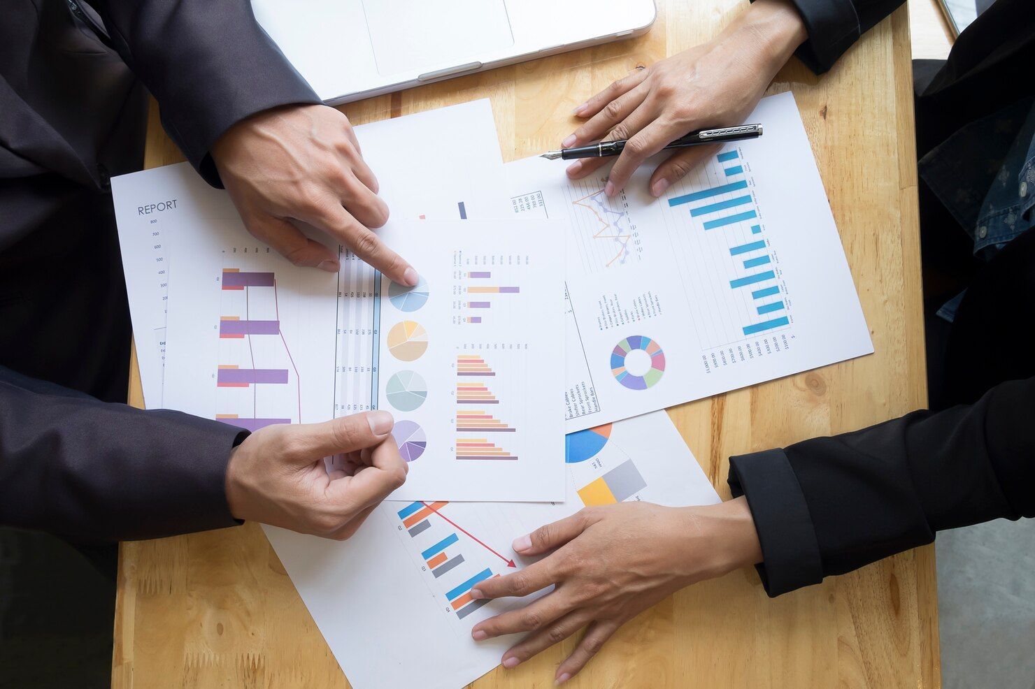 Hands reviewing printed charts and graphs on a wooden table during a business meeting