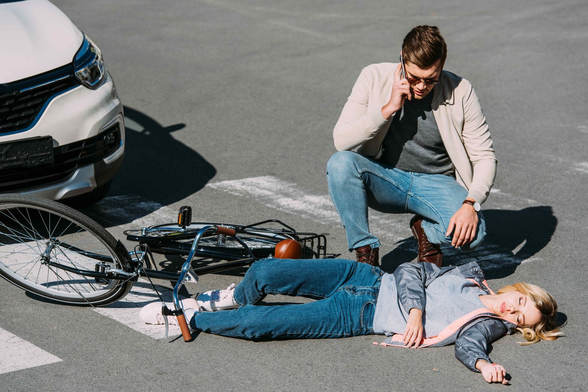 A male driver on the phone, kneeling to a female bicyclist who is lying on the street unconscious. Clicking this picture takes you to Bicycle Accidents.