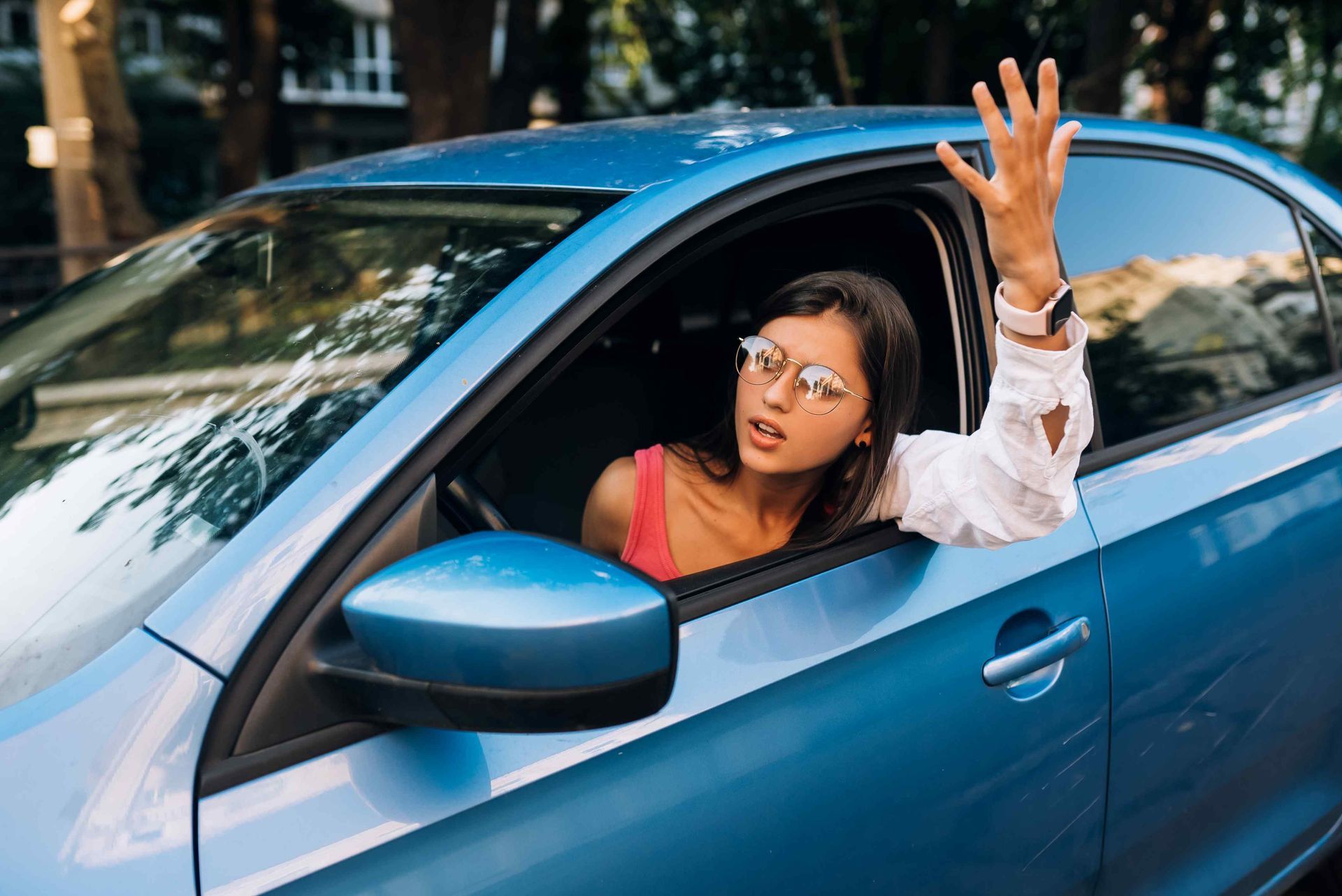 A female driver leaning out of the driver-side window with her hand raised wondering what happened in 