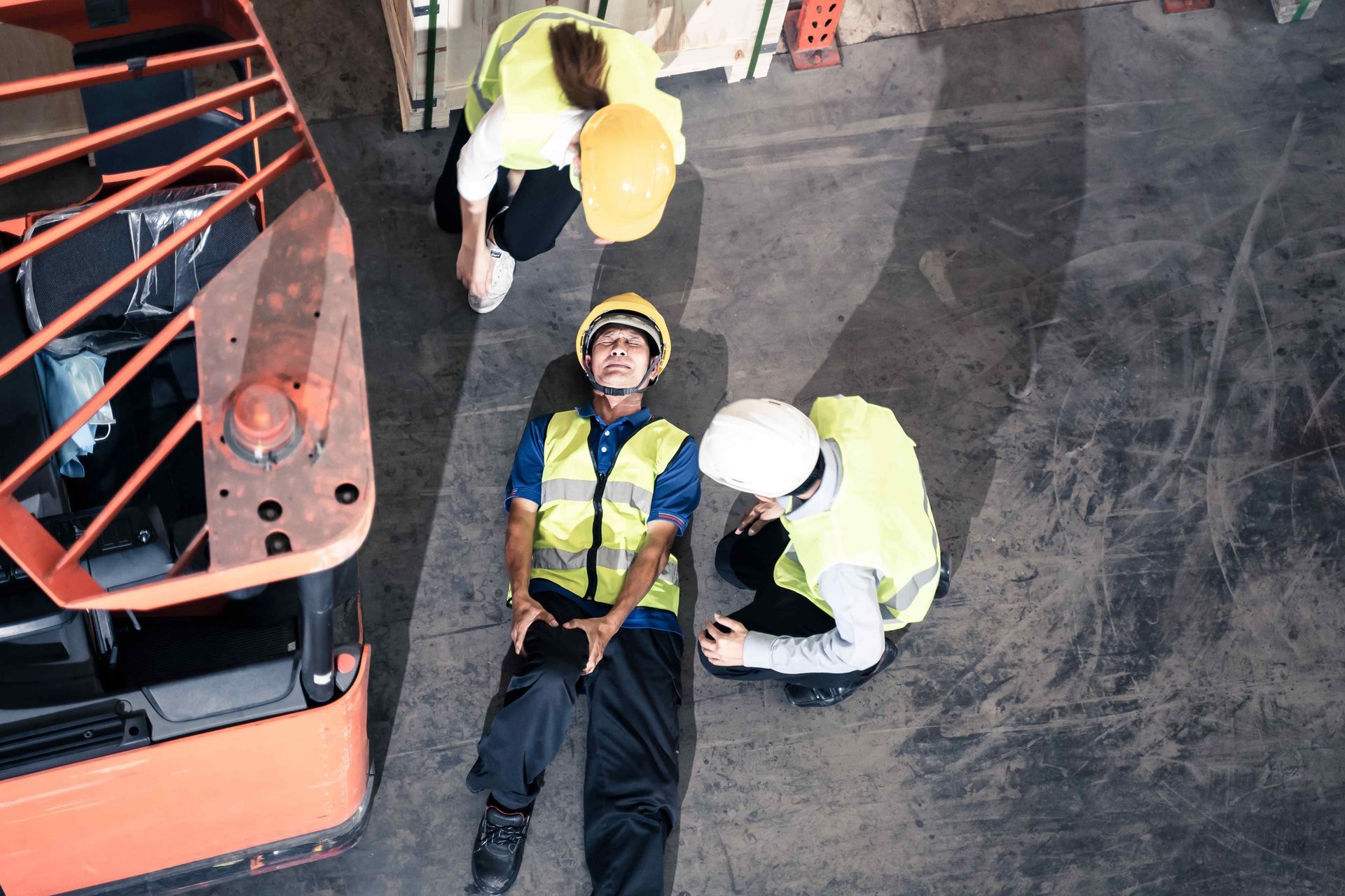 A worker lying on the ground holding their knee close to them, surrounded by two other workers after getting injured in the workplace.  Clicking this picture takes you to Workplace Accidents.