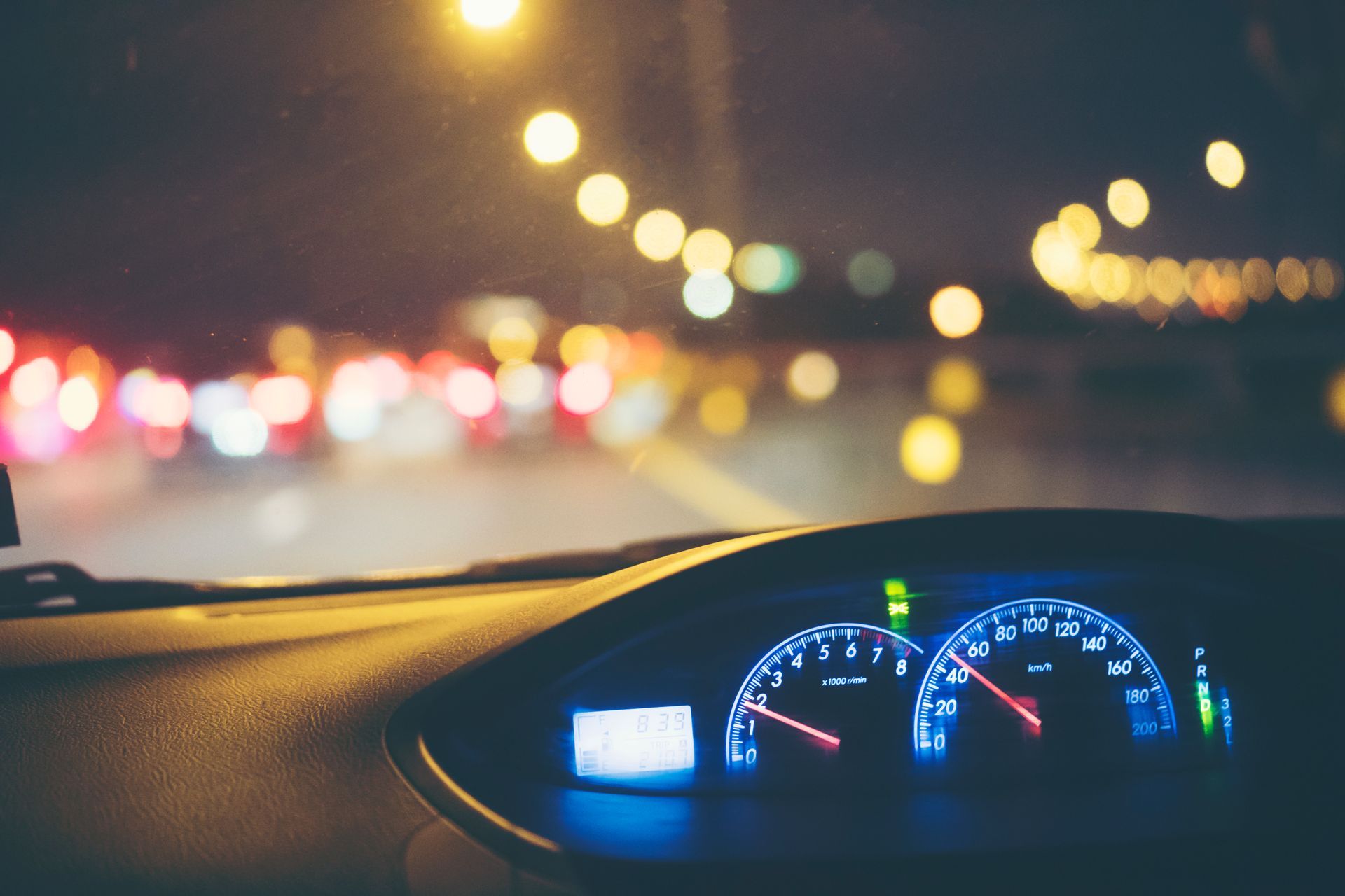 Driver’s dashboard view of nighttime traffic with blurred city lights and reduced road visibility