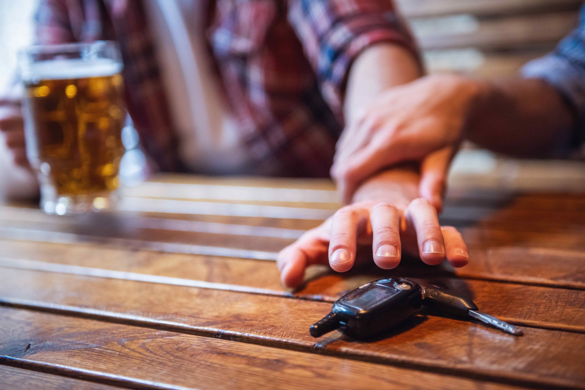 Person reaching for car keys next to alcoholic drink at bar, highlighting dangers of drinking and driving
