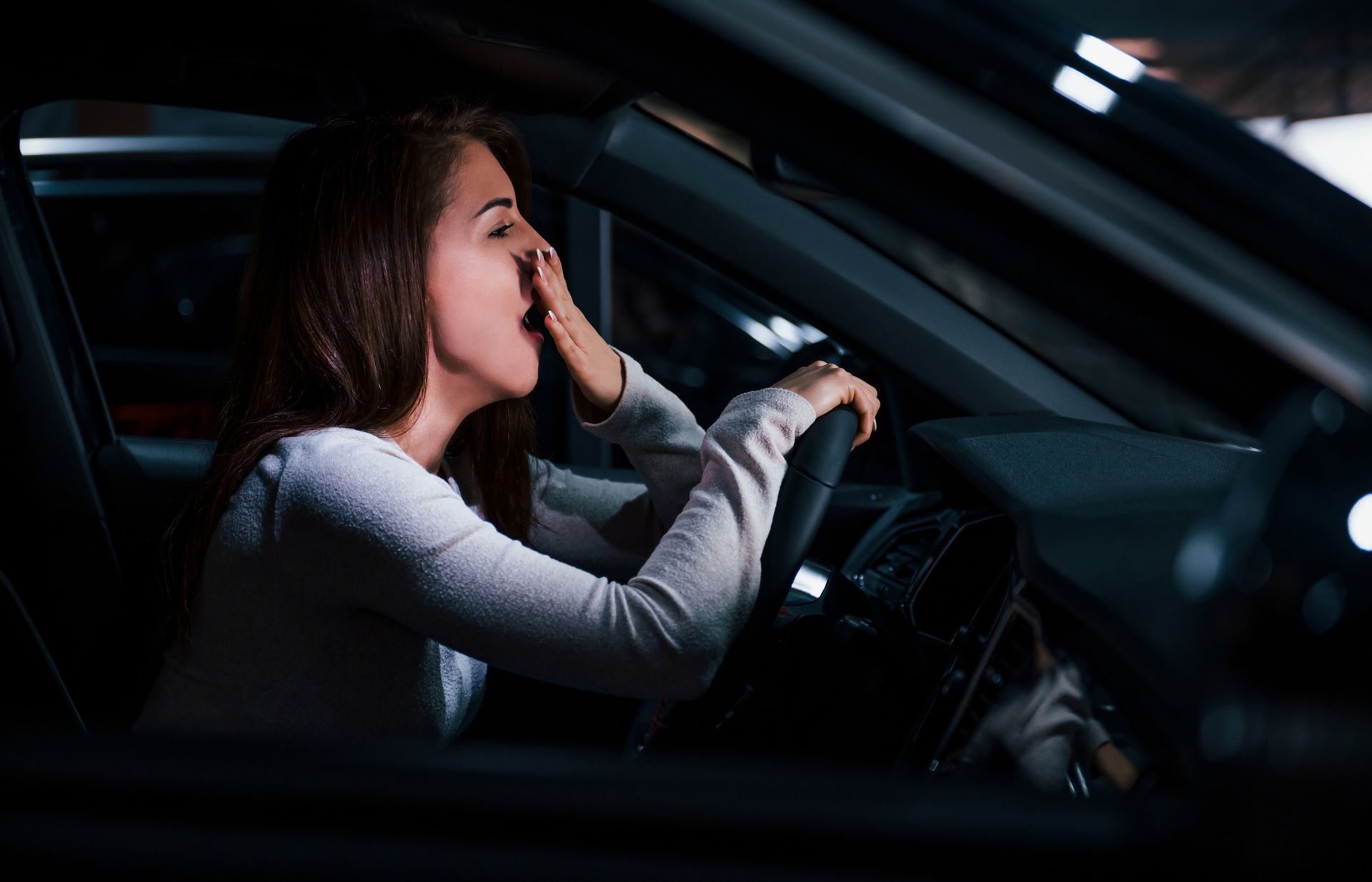 Fatigued driver yawning behind the wheel during nighttime driving, demonstrating dangers of drowsy driving
