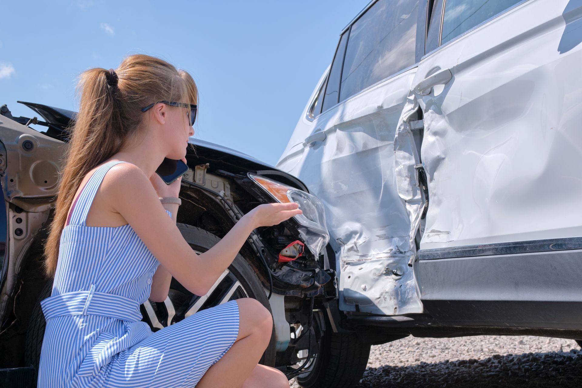 Driver talking on a cell phone while inspecting significant side damage to a vehicle after a traffic