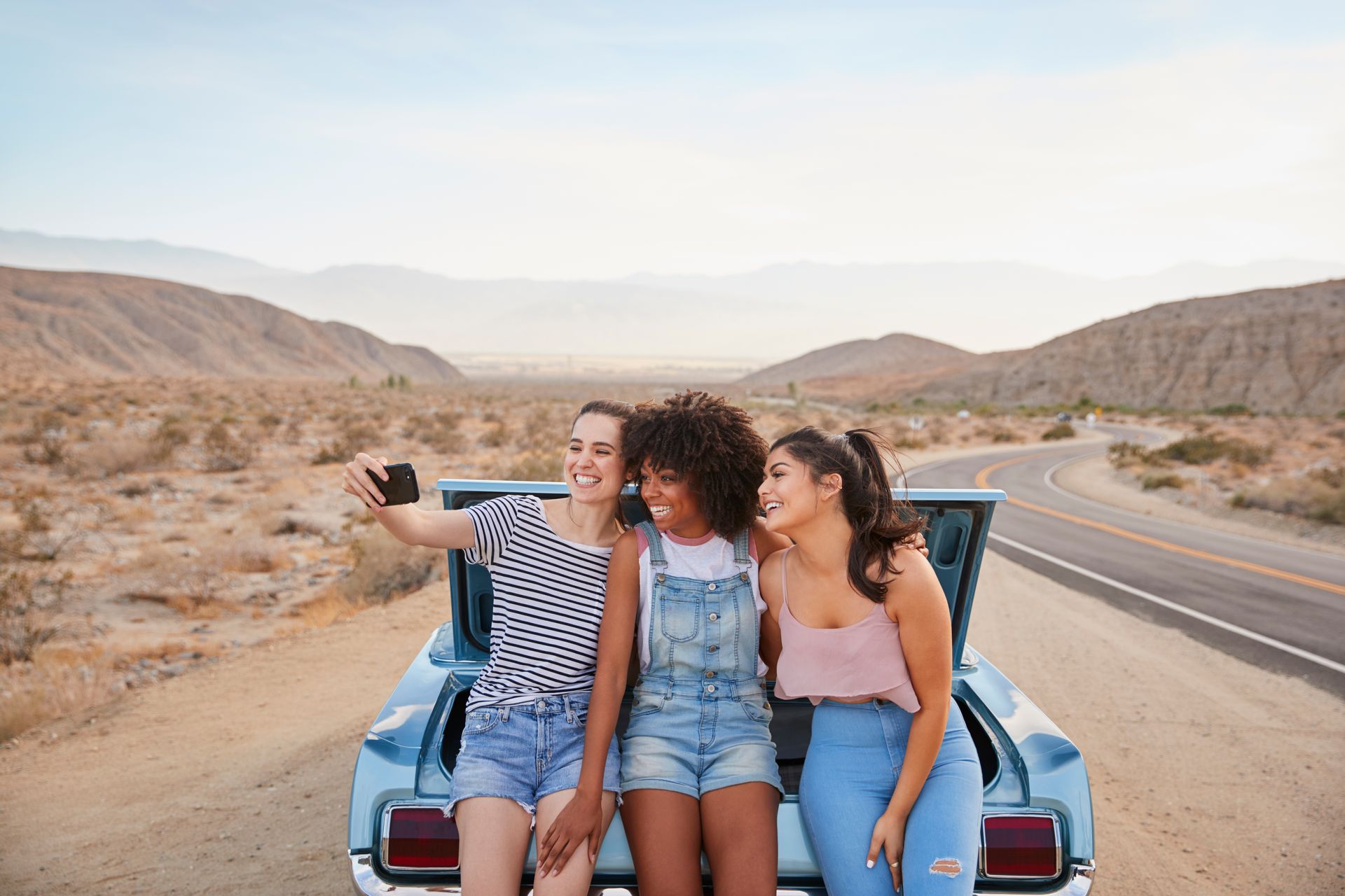 Friends taking selfie during Arizona desert road trip, summer travel and driving safety awareness