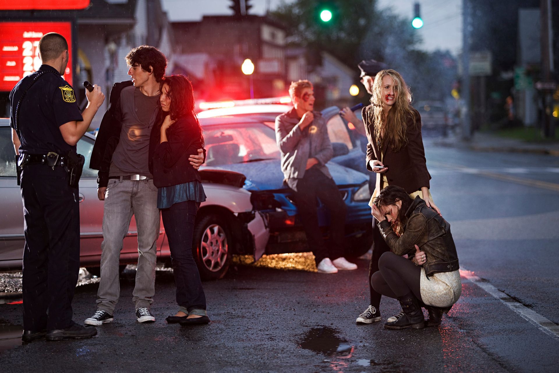 Police officer speaking with people involved in a nighttime vehicle accident while damaged cars and emergency lights illuminate the crash scene.