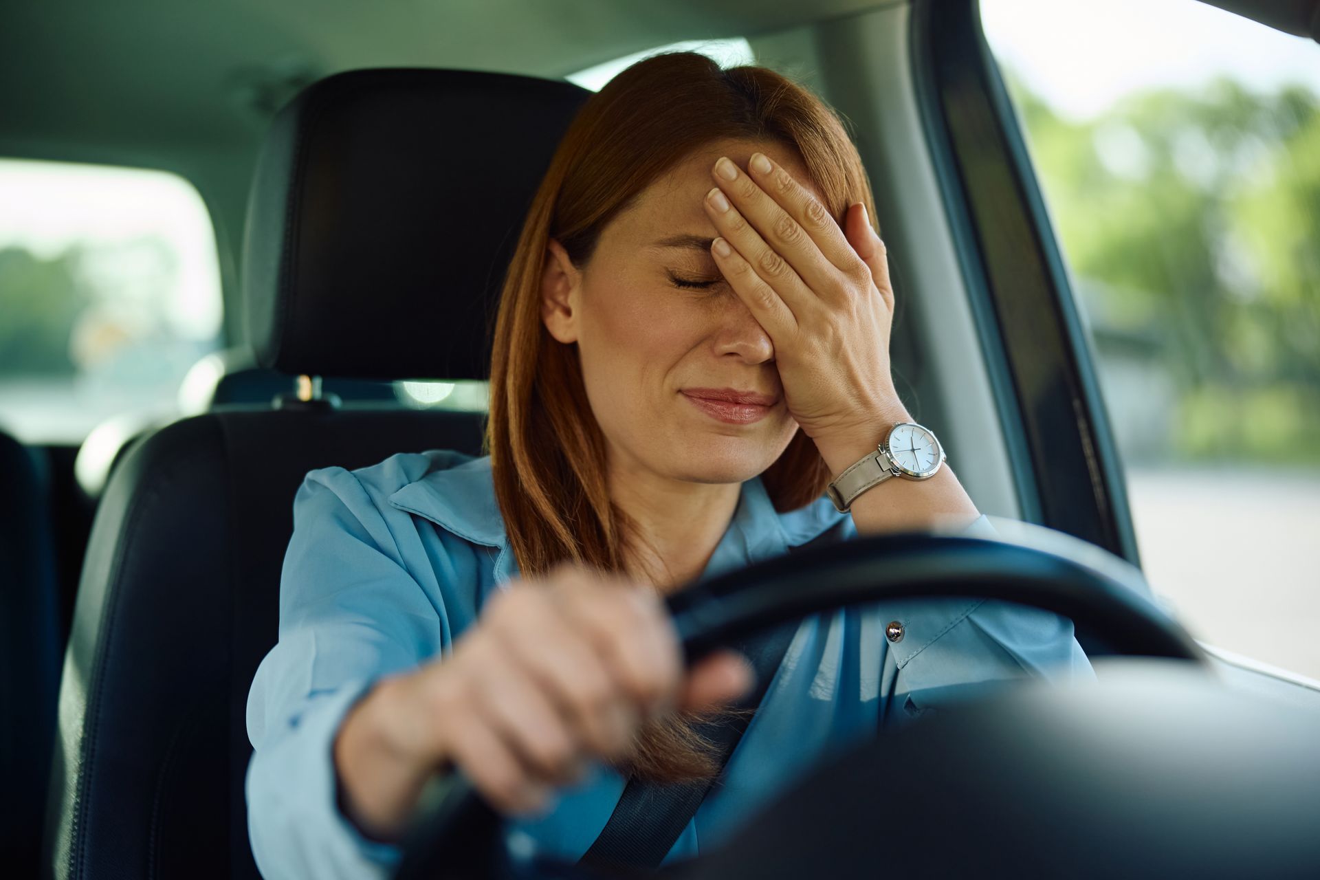Upset driver covering her face behind the wheel, representing emotional stress, anxiety, and mental health challenges following an accident.