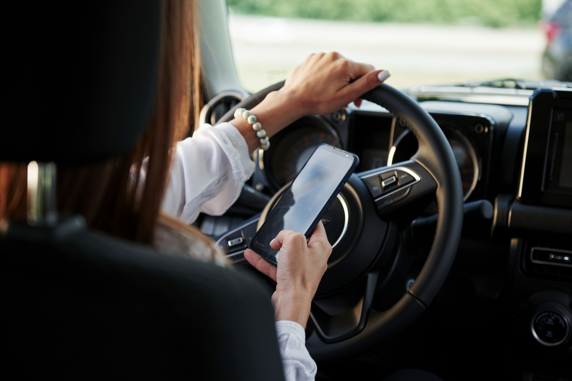 Woman using smartphone while driving vehicle, demonstrating distracted driving dangers and increased