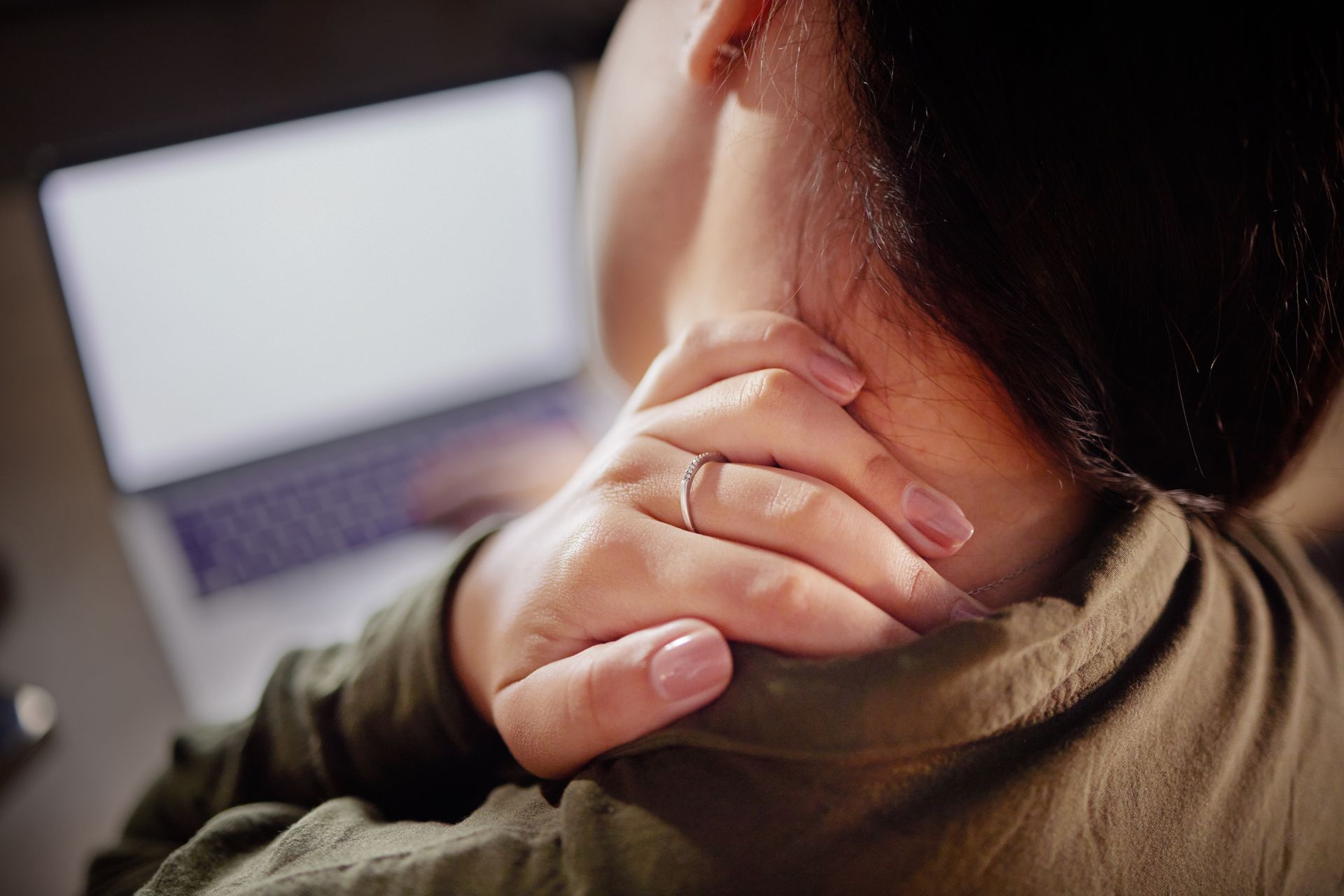 Woman rubbing her neck while using a laptop, showing neck pain and whiplash-related discomfort.