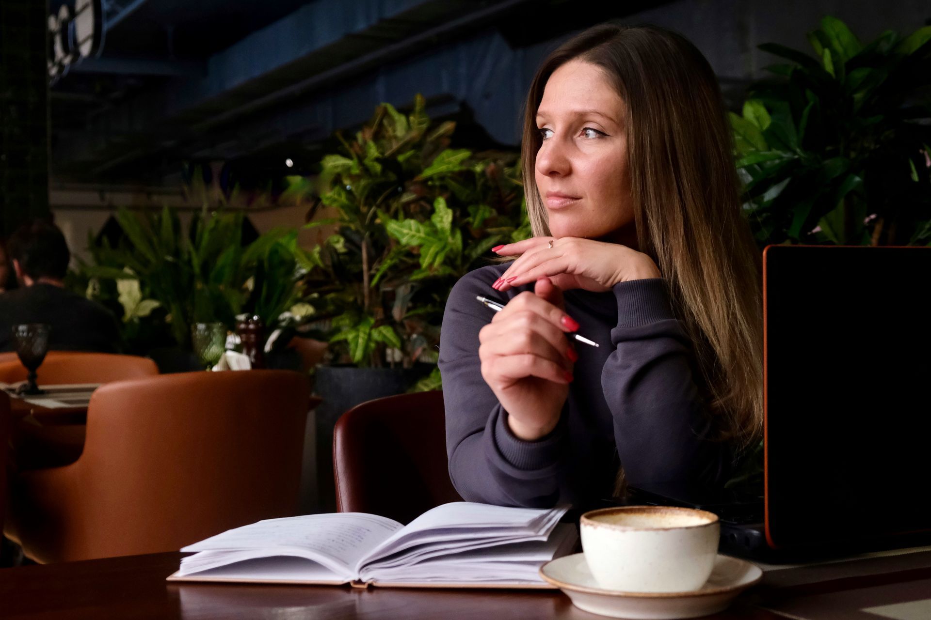 Woman reflecting while working at a table with a notebook and coffee, representing emotional recovery, self-reflection, and coping after a traumatic experience.