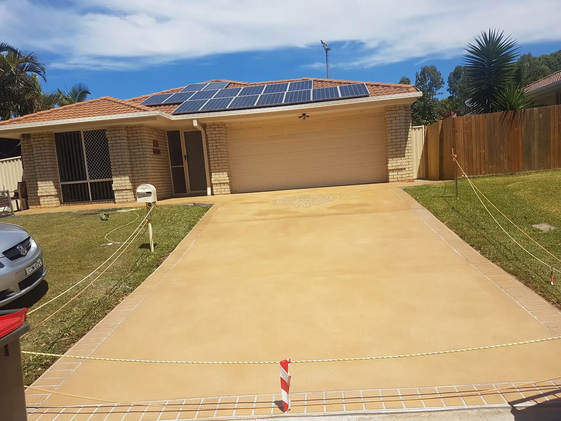 House with solar panels, a beige garage door, and a concrete driveway on a sunny day.