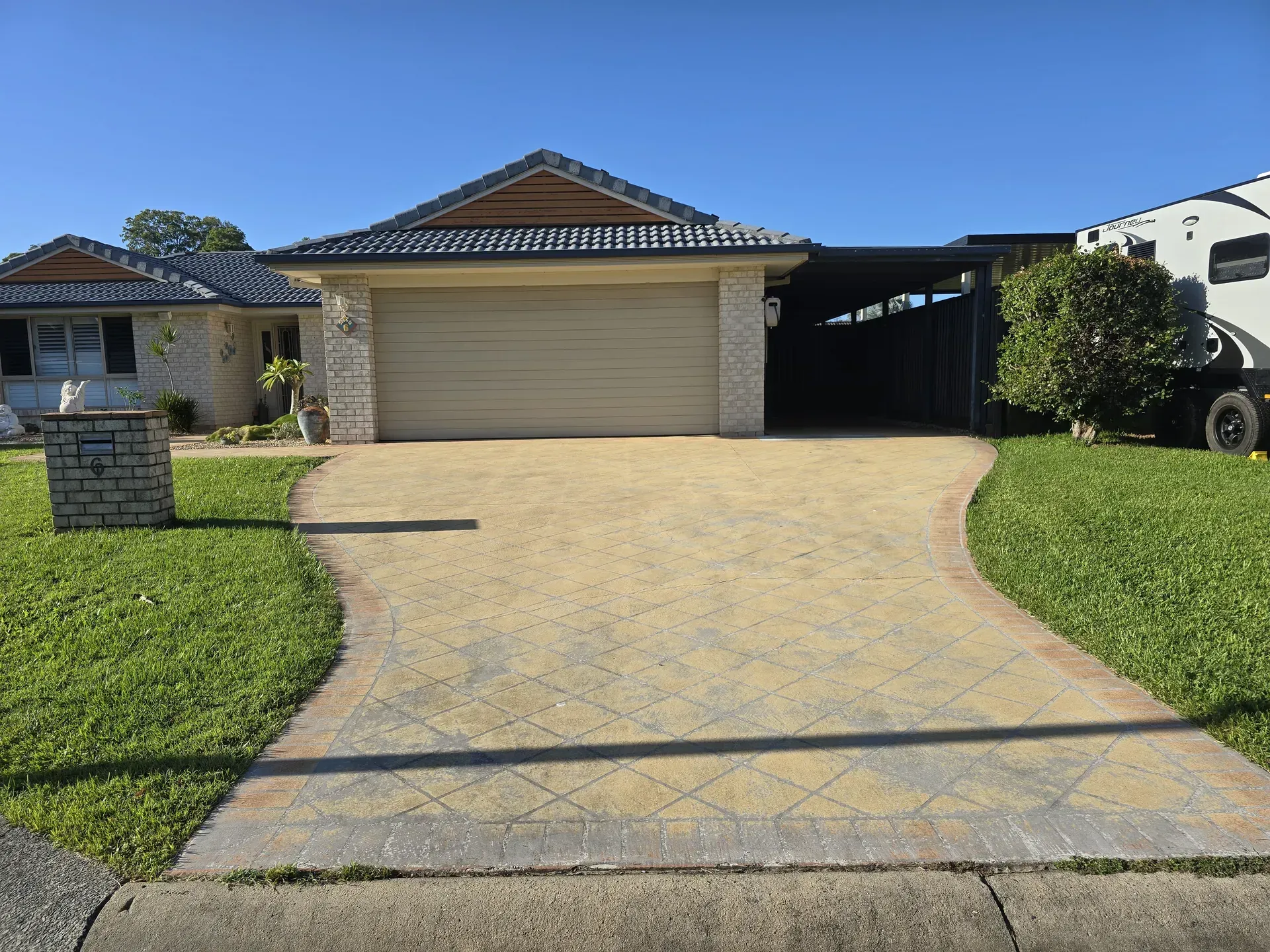 House with driveway leading to a garage and carport on a sunny day. Green lawn and blue sky.