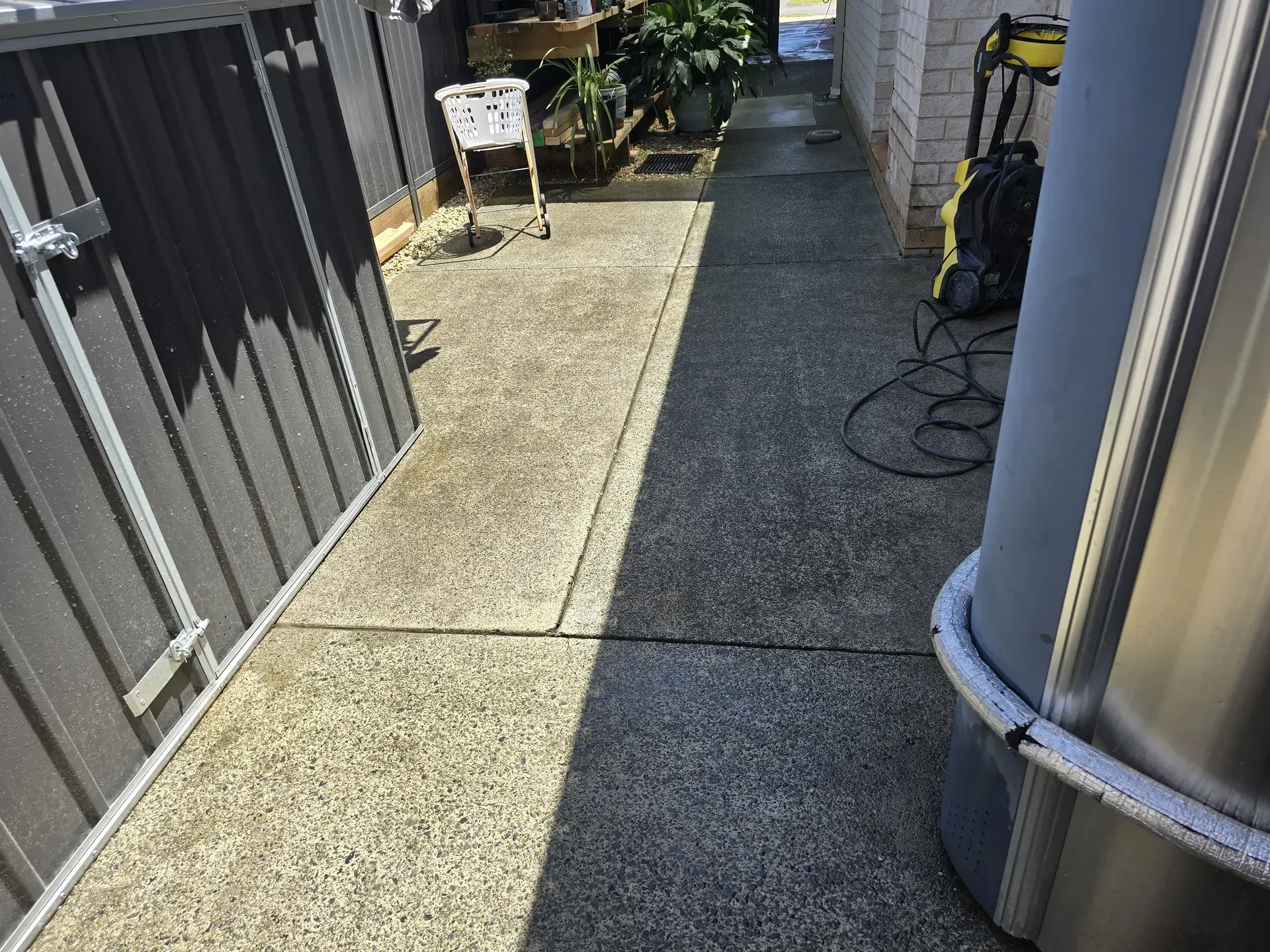 Tan concrete pathway next to brick building and lawn, in front of a house.