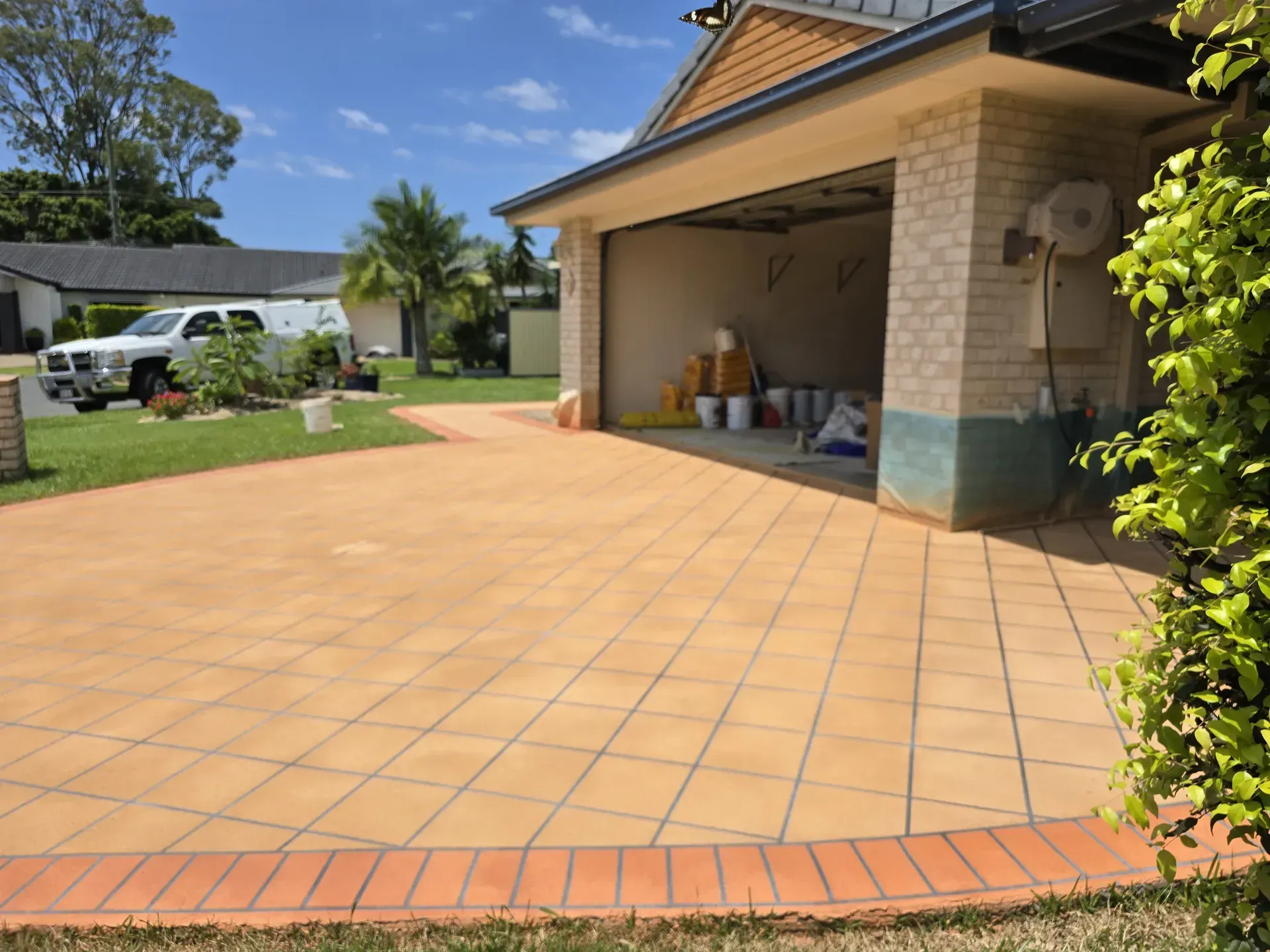 Driveway with brick border leads to a garage. Driveway is orange-tiled. A white truck is in the distance.