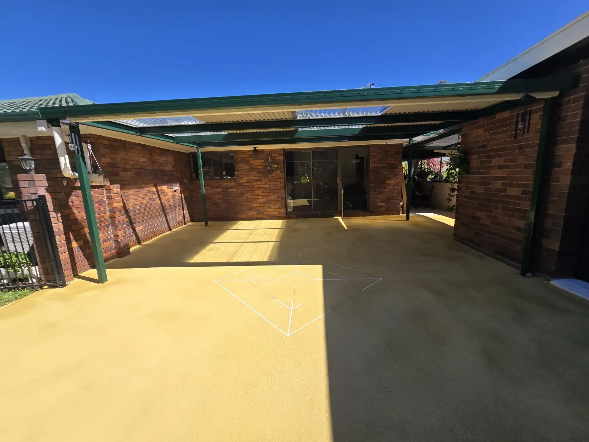 Covered carport with yellow floor, red brick walls, and glass doors against a clear blue sky.
