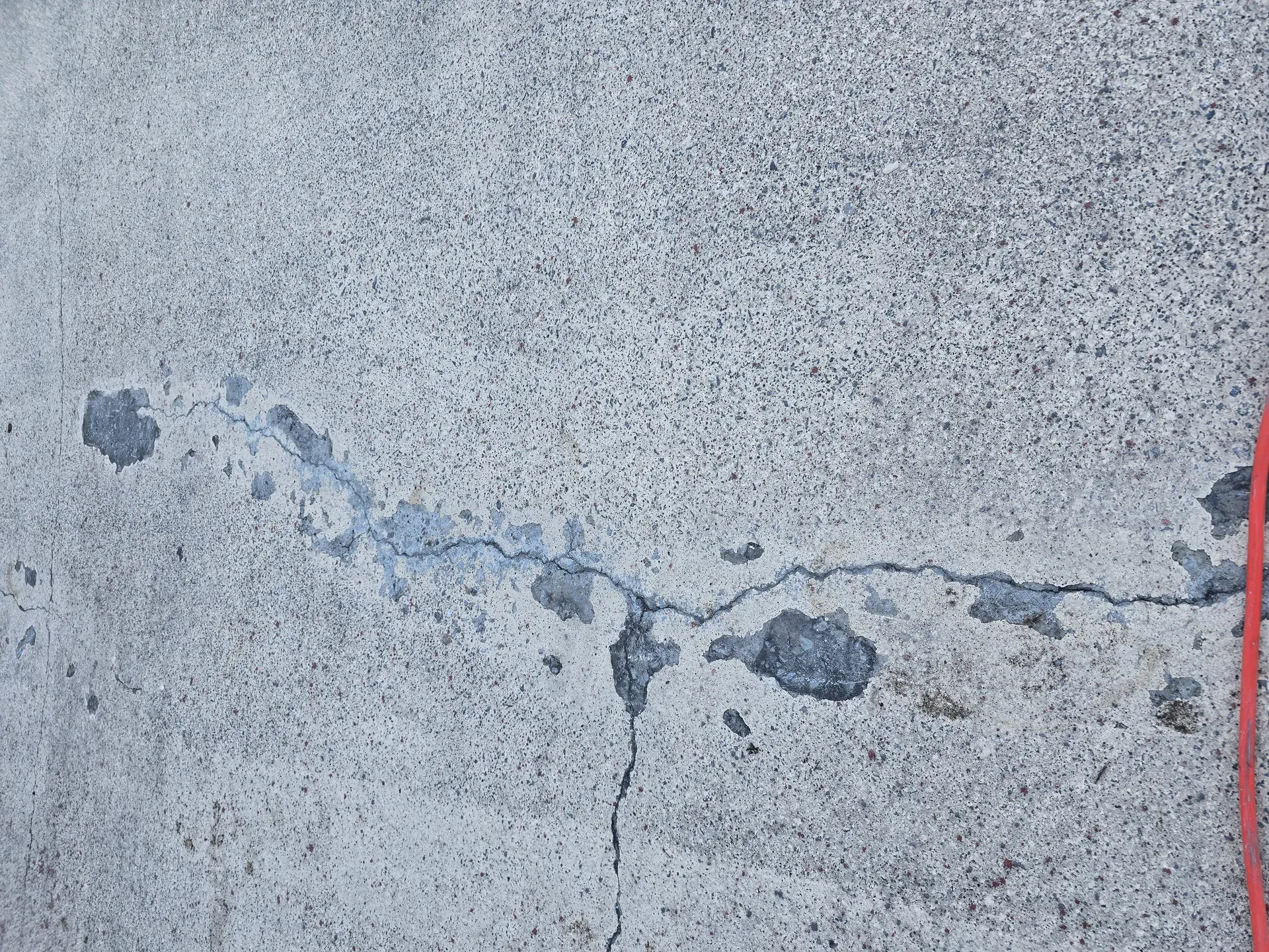 Cracked concrete surface with patches and a red vertical line.