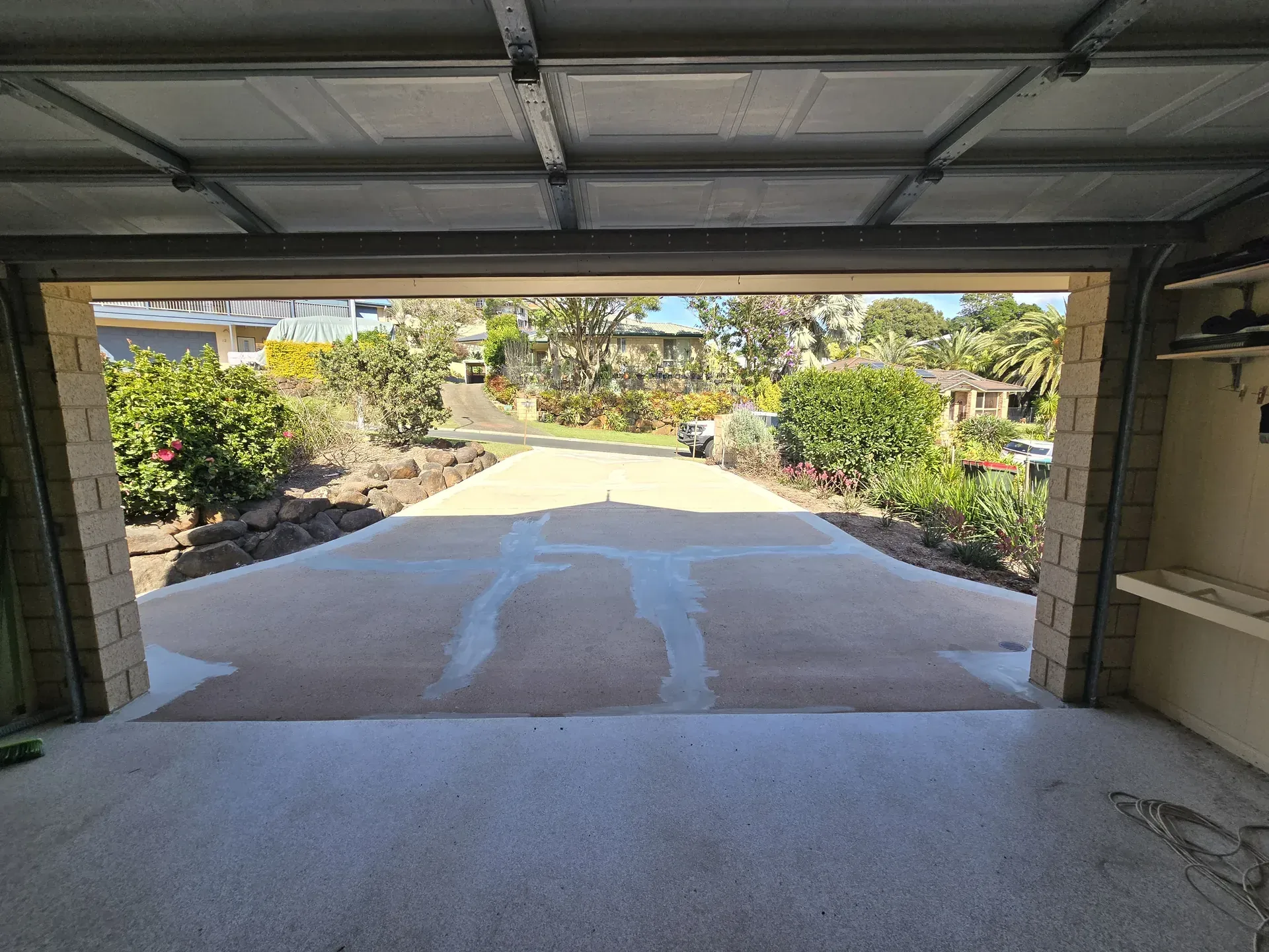 View from inside a garage looking out at a driveway and landscaping; sunlight.