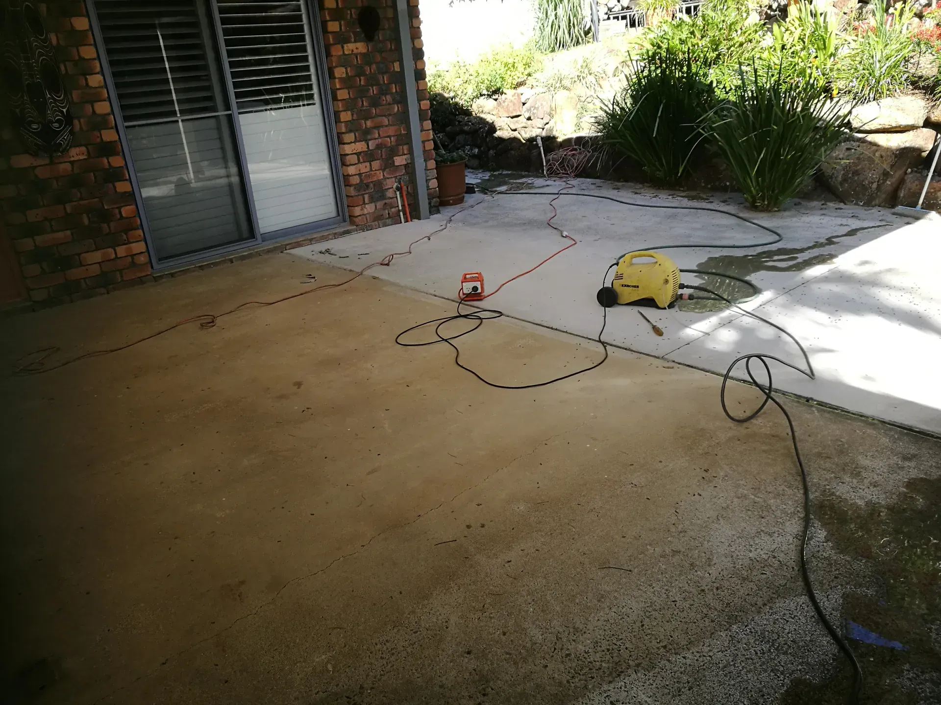 Concrete patio being cleaned with a pressure washer; cord and equipment visible.