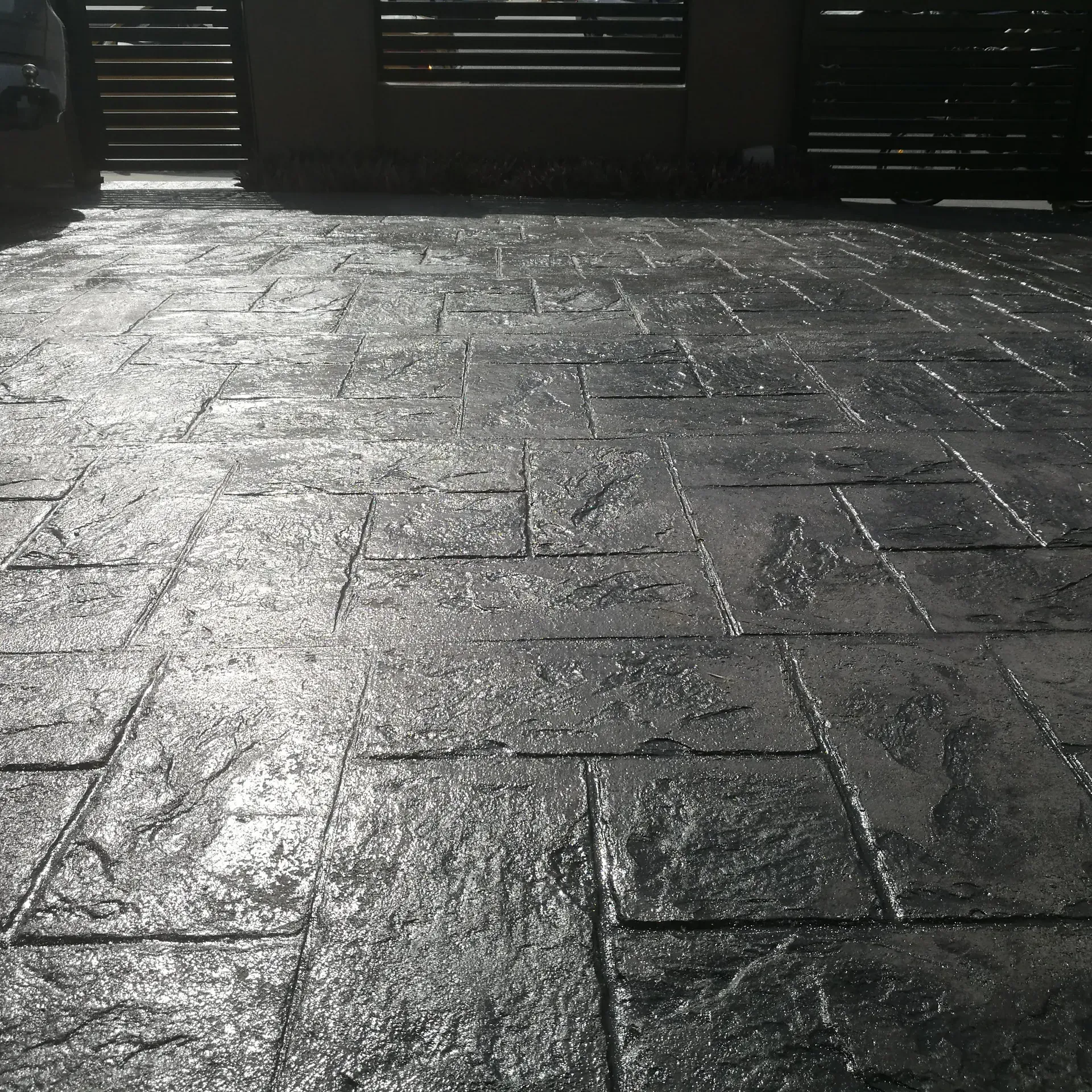 Dark gray stamped concrete patio with sunlight. A dark metal gate is in the background.