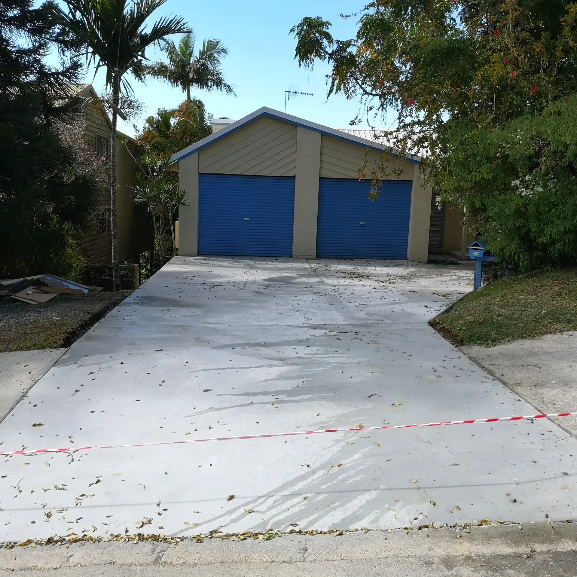 Concrete driveway leading to a two-car garage with blue doors; trees and a blue sky in the background.