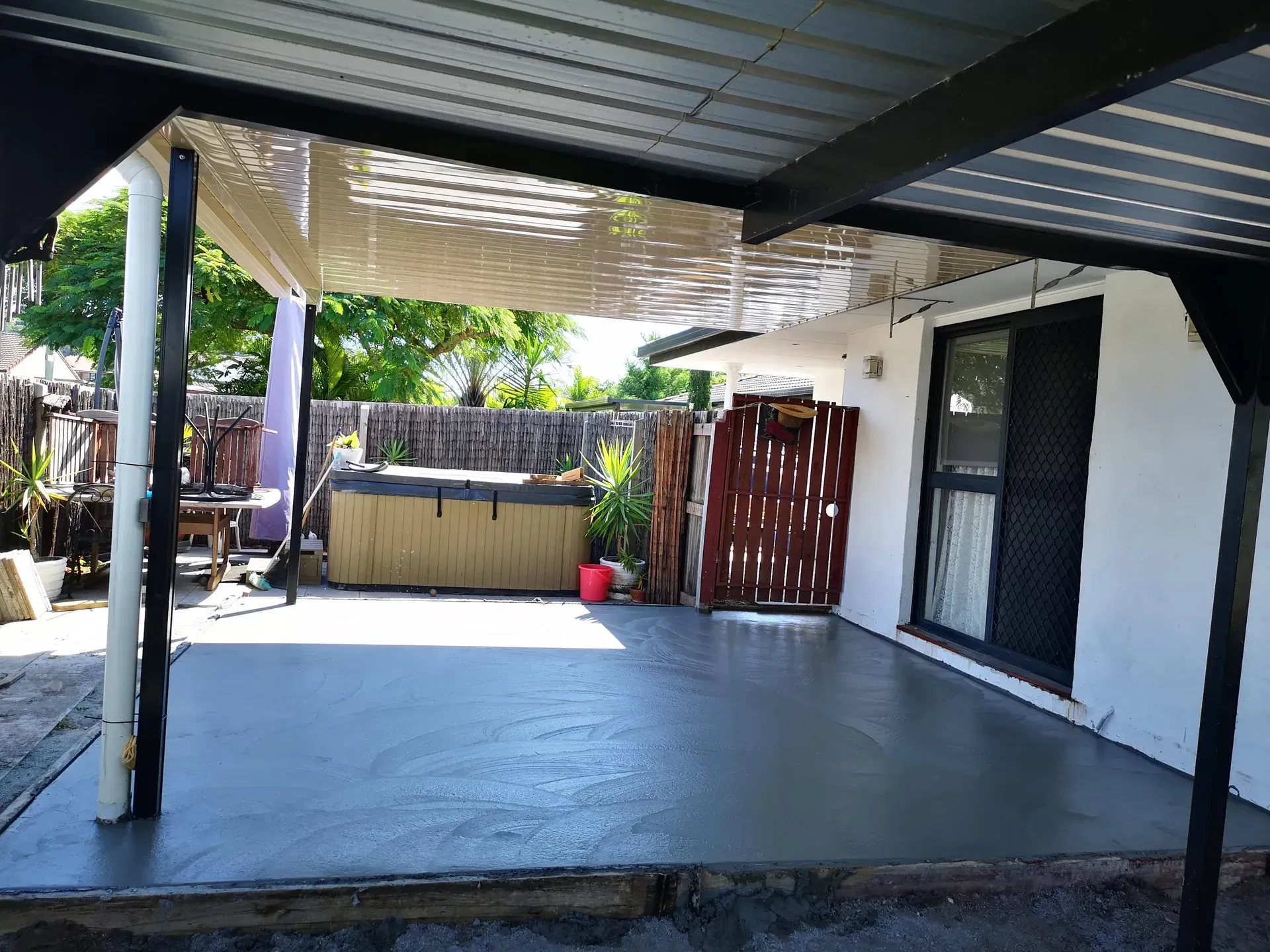 Covered patio with a concrete floor, next to a white house with a sliding glass door.